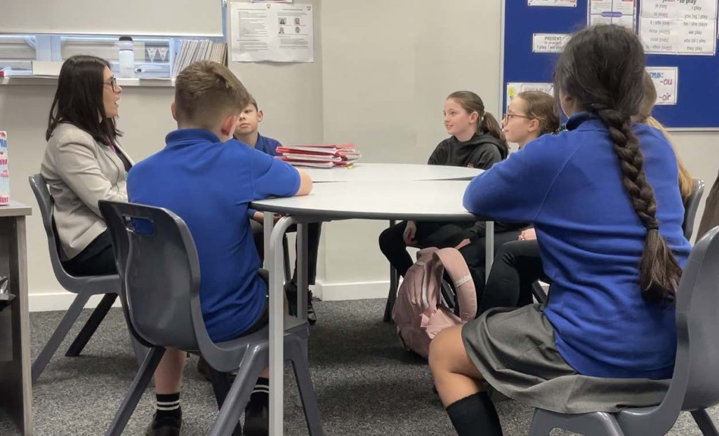 Group session with six children sitting around the table with school staff member