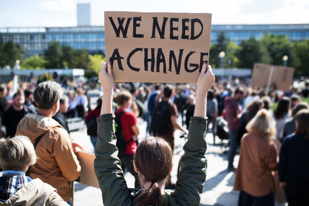 Person holding cardboard sign that reads "We need a change"